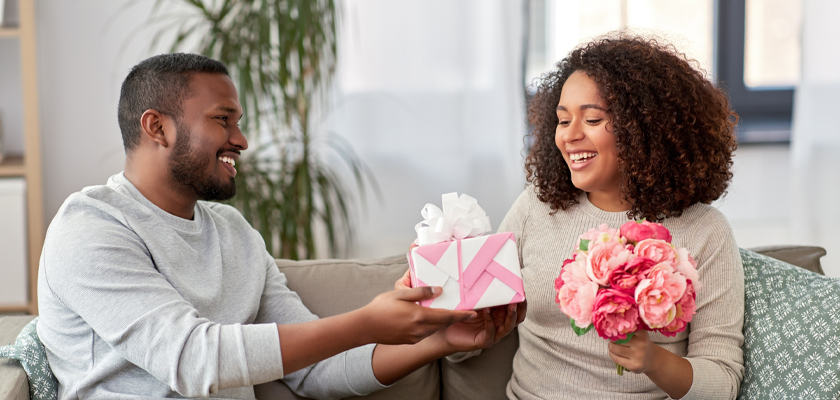 A joyful couple exchanges a beautifully wrapped gift and a bouquet of flowers, celebrating love.