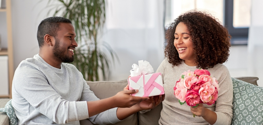 A joyful couple exchanges a beautifully wrapped gift and a bouquet of flowers, celebrating love.