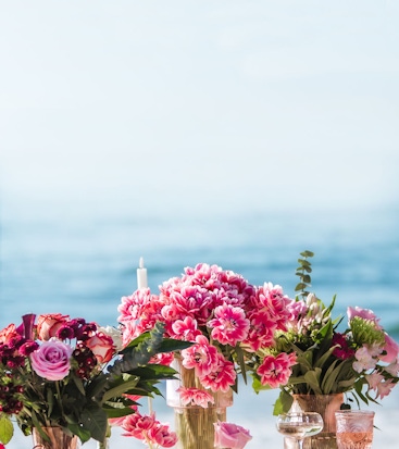 Vibrant floral arrangements featuring pink and red blooms by the ocean, ideal for events.