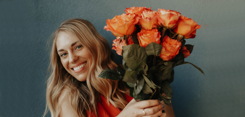 A smiling woman holding a vibrant bouquet of orange roses, showcasing joy and beauty.
