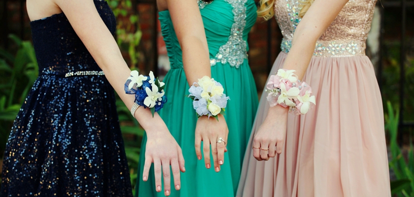 Three elegantly dressed girls display colorful wrist corsages, complementing their stunning gowns.