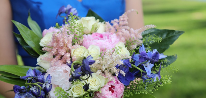 A vibrant bouquet featuring pink peonies, blue delphiniums, and delicate greenery.