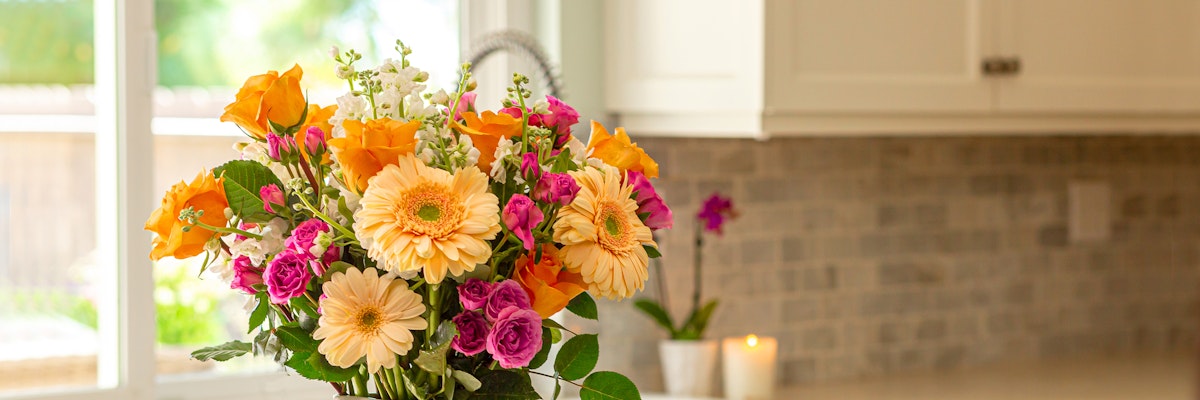 Vibrant floral arrangement featuring yellow gerbera daisies and pink roses on a kitchen counter.