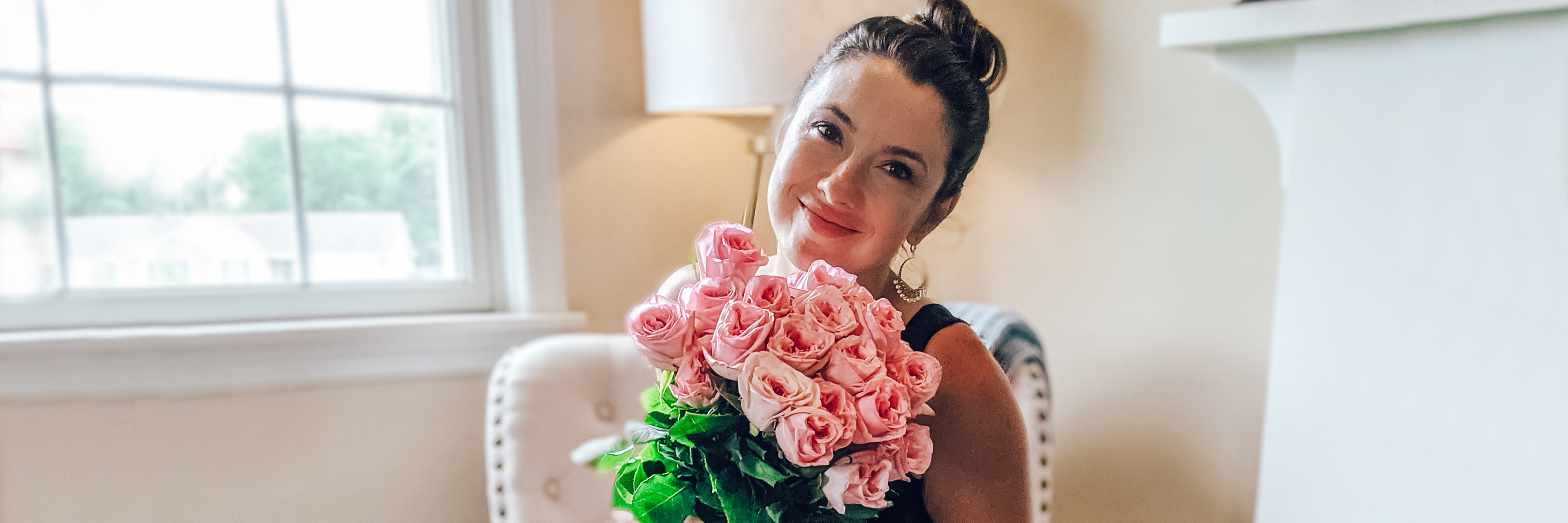 A woman holding a vibrant bouquet of pink roses, smiling joyfully in a cozy setting.