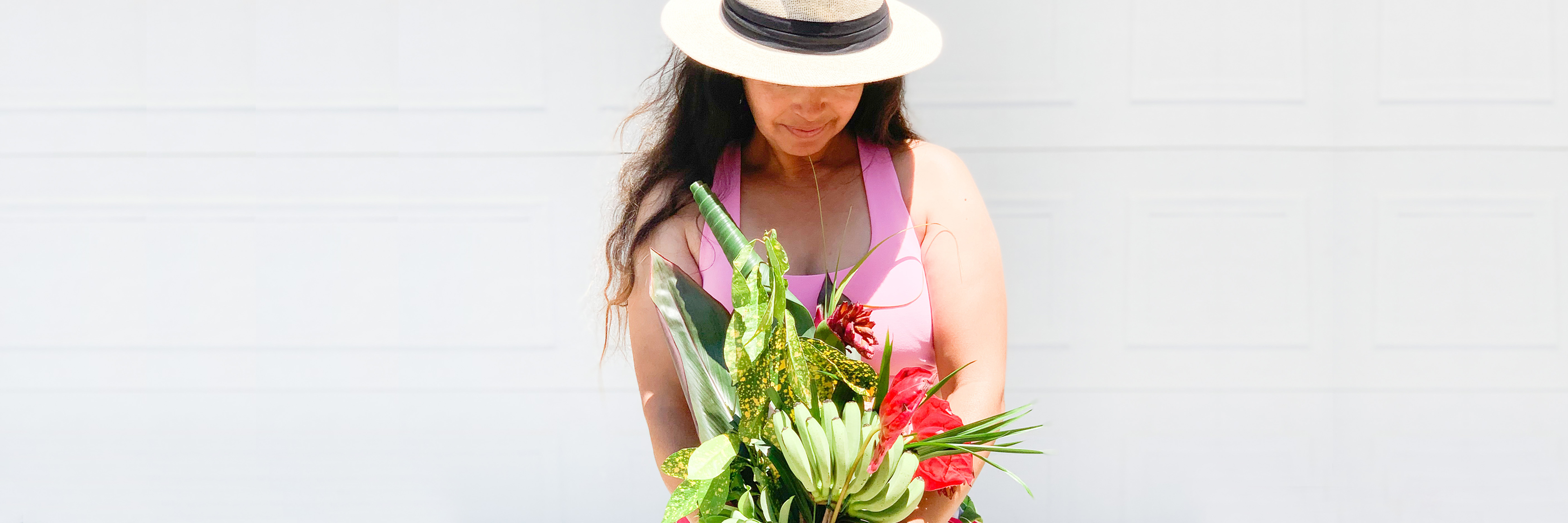 A woman in a pink top holds a vibrant floral bouquet with tropical accents.