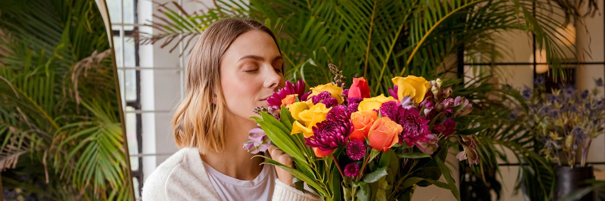 A woman gently embraces a vibrant floral bouquet, surrounded by lush greenery, exuding joy.