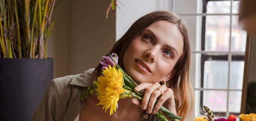 A thoughtful young woman delicately holds vibrant yellow flowers, smiling gracefully.