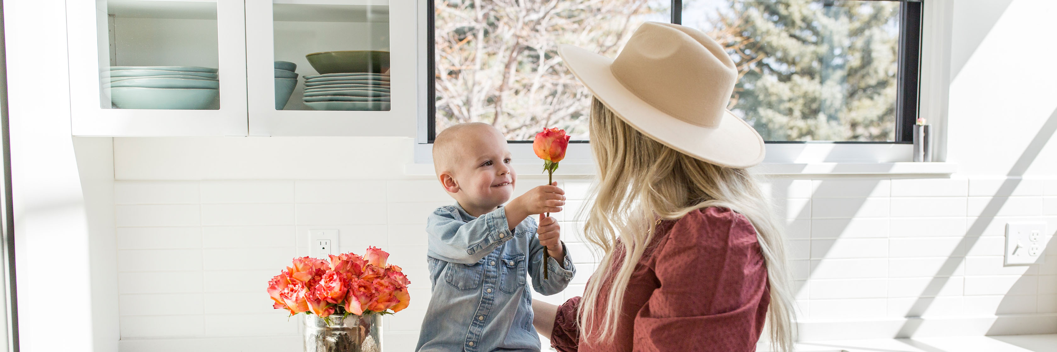 A joyful scene of a mother and child sharing a flower in a bright kitchen.