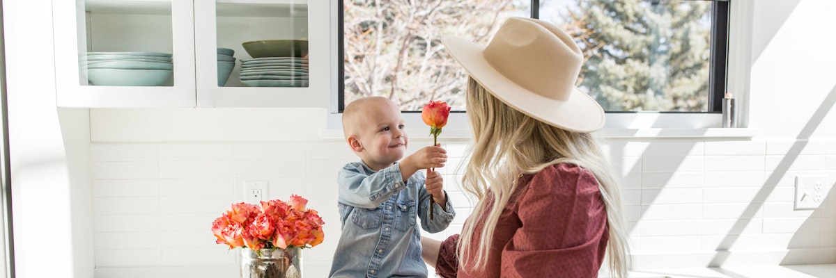 A joyful scene of a mother and child sharing a flower in a bright kitchen.