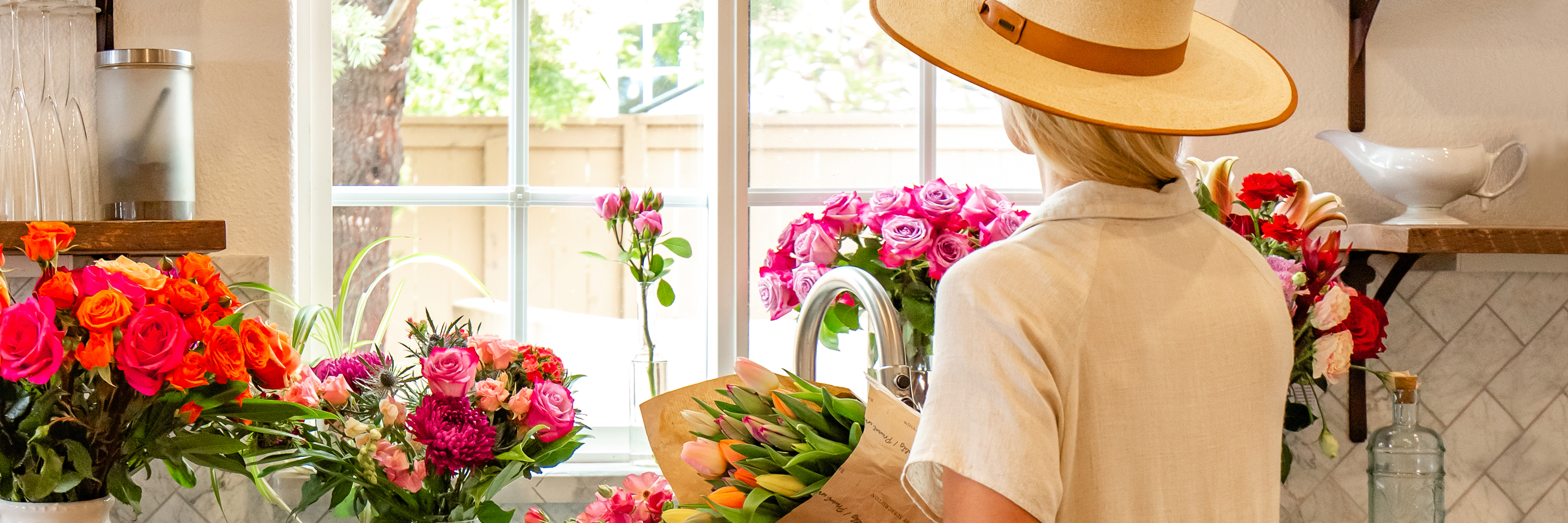 A florist arranging vibrant flowers in a bright, sunny kitchen setting.