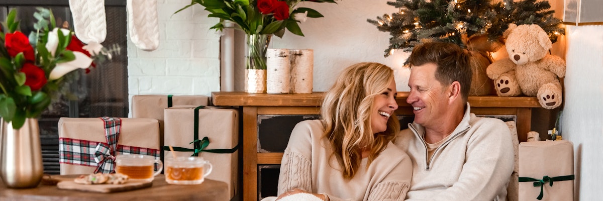 Cozy couple enjoying holiday vibes by a fireplace with gifts and festive decor.