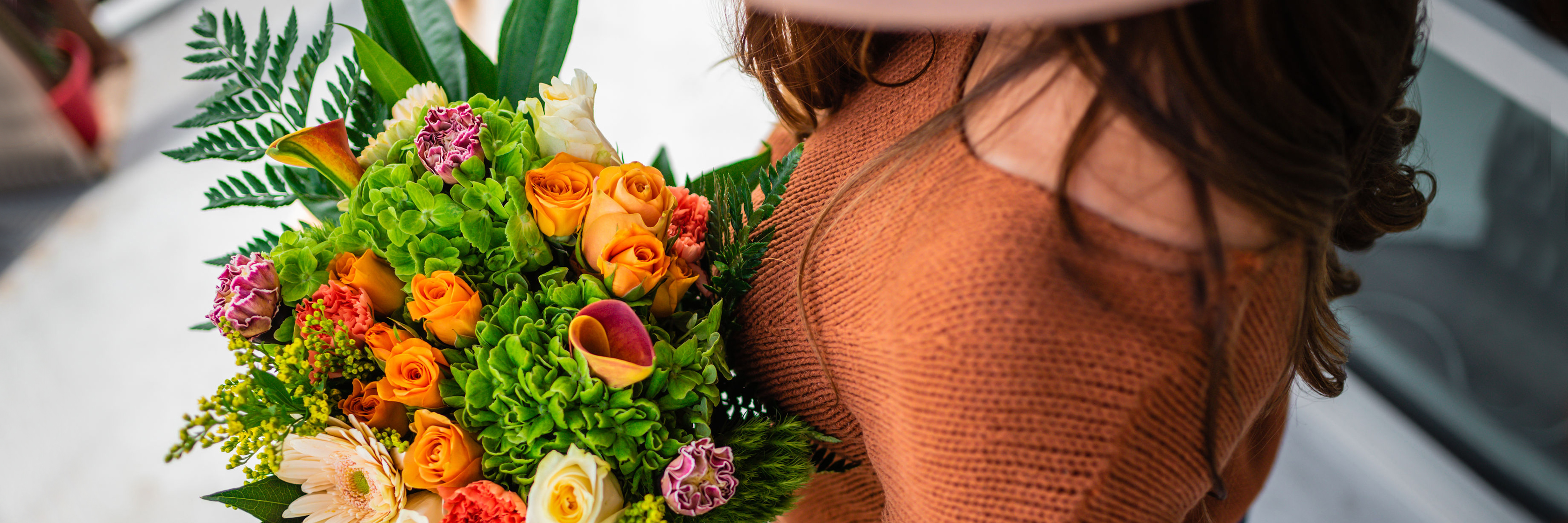 Vibrant bouquet featuring orange roses, green hydrangeas, and colorful blooms, held by a woman.