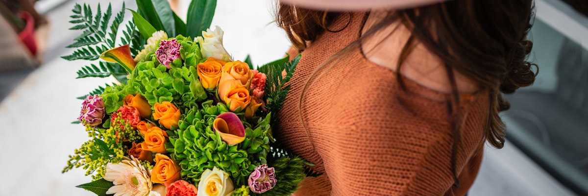 Vibrant bouquet featuring orange roses, green hydrangeas, and colorful blooms, held by a woman.