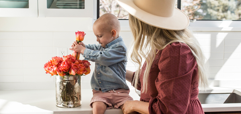 A child and a woman enjoy a beautiful bouquet of roses in a modern kitchen setting.
