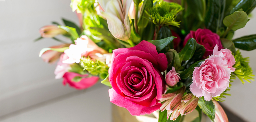 Vibrant floral arrangement featuring pink roses, lilies, and greenery in a rustic vase.