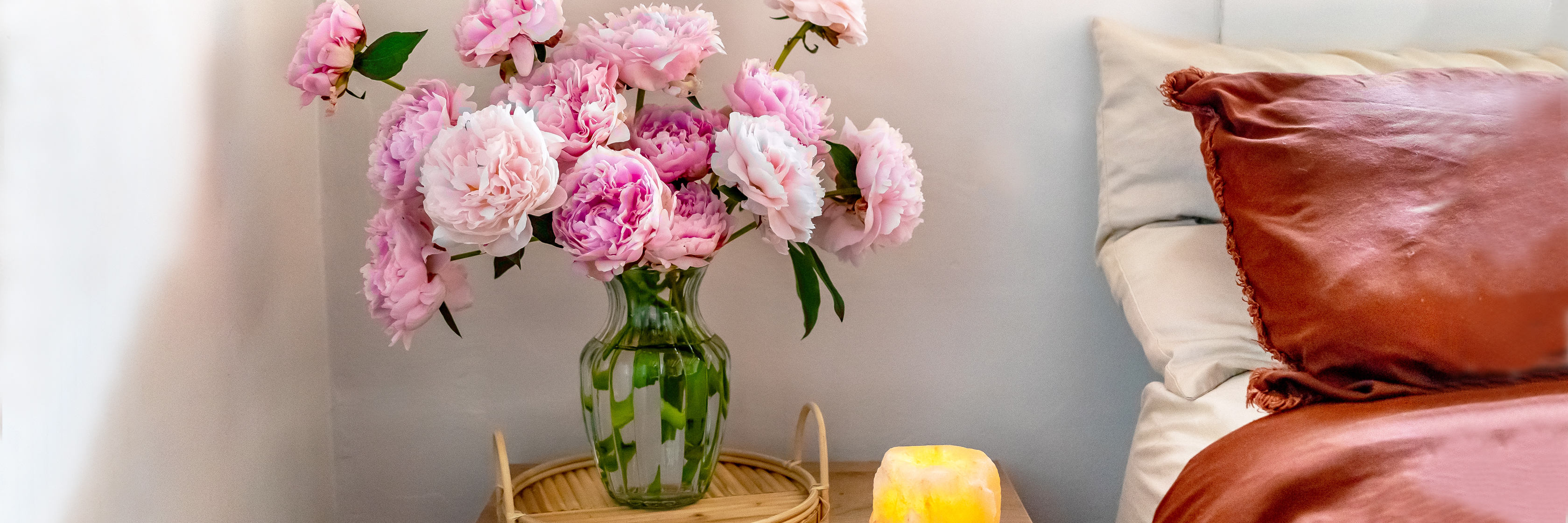 A charming vase filled with pink peonies on a bedside table, complemented by soft bedding.