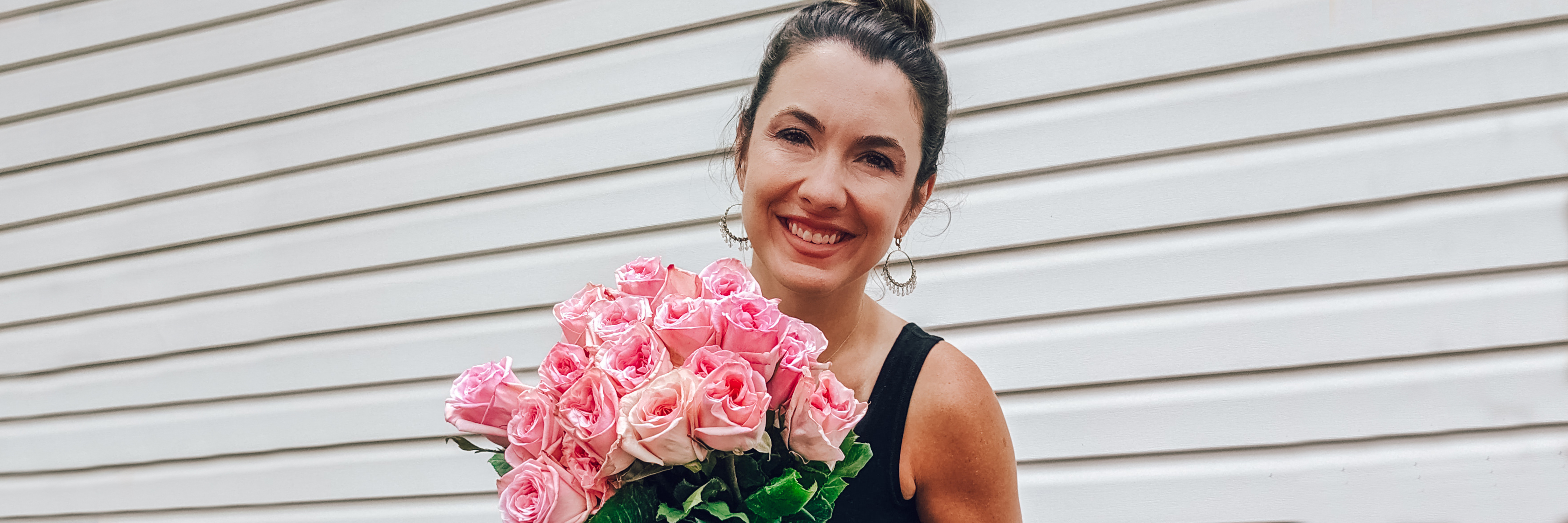 A smiling woman holds a stunning bouquet of pink roses against a light backdrop.
