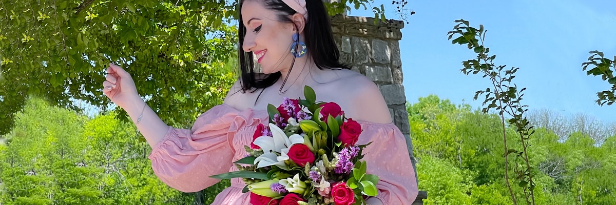 A joyful woman in a pink dress holds a vibrant floral bouquet amidst lush greenery.