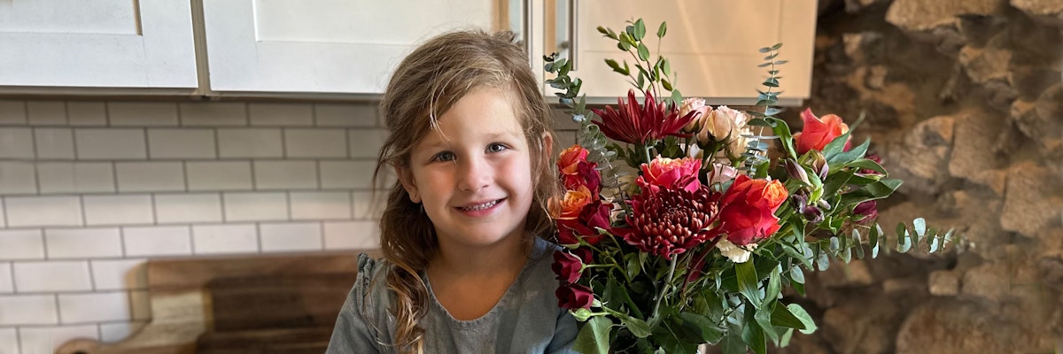 A smiling young girl holding a vibrant bouquet of mixed flowers in a cozy kitchen setting.
