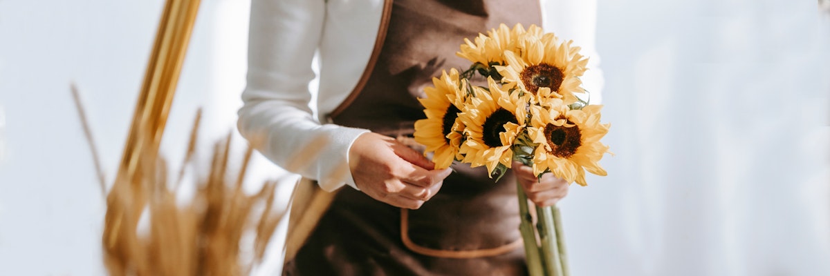 A creative florist in an apron holding a vibrant bouquet of sunflowers, ready for arrangement.