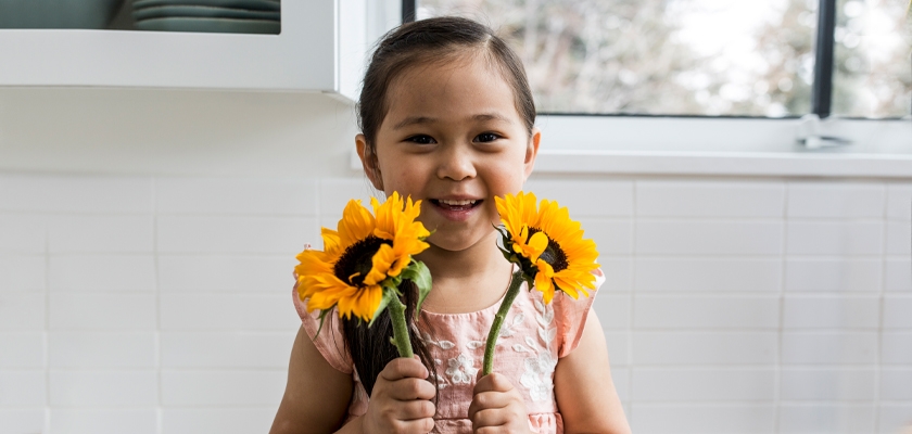 Young girl joyfully holding bright sunflowers in a cheerful kitchen setting.