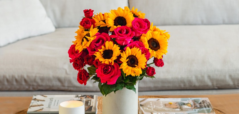 A vibrant arrangement of sunflowers and pink roses in a stylish vase on a cozy table.