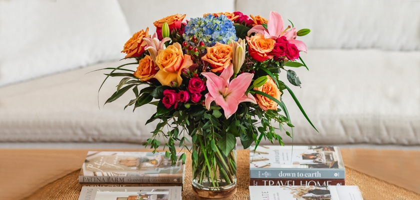 Vibrant floral arrangement featuring orange roses, lilies, and colorful blooms in a glass vase.
