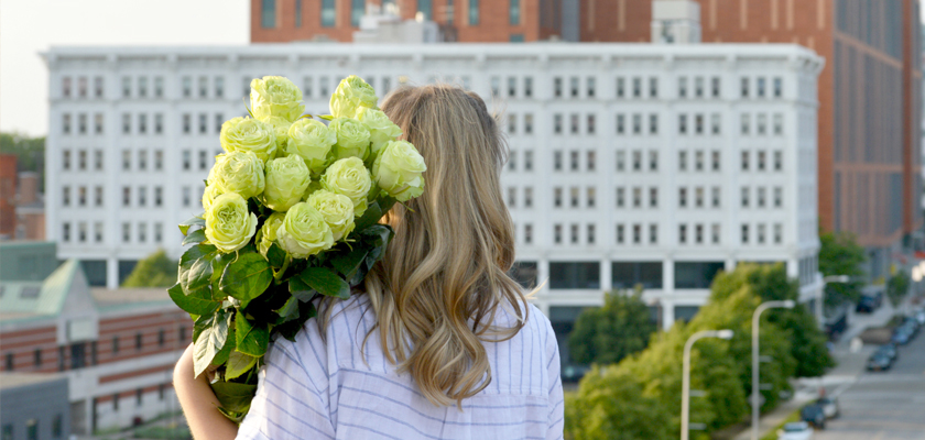 A woman holding a bouquet of pale green roses against a city backdrop, showcasing elegance.