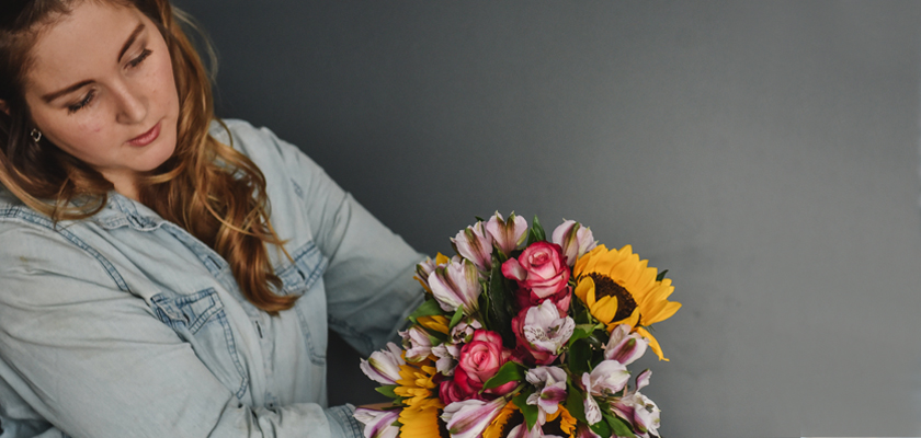 A woman arranging a vibrant floral bouquet featuring sunflowers and pink roses.
