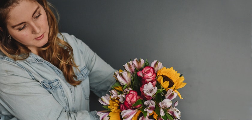 A woman arranging a vibrant floral bouquet featuring sunflowers and pink roses.