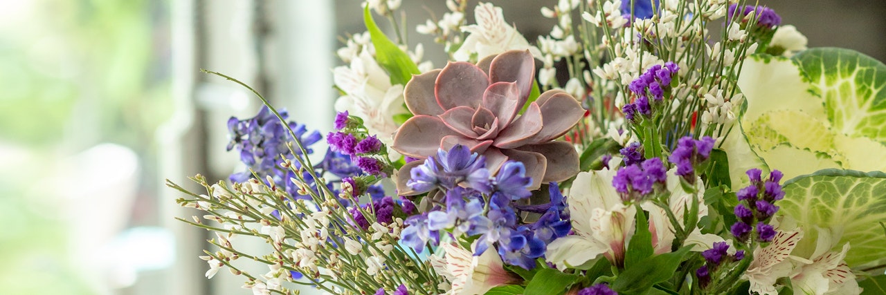 A vibrant floral arrangement featuring purple flowers, succulents, and lush greenery.