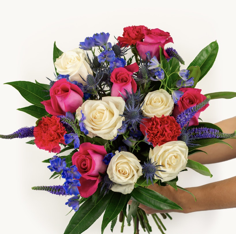 A vibrant bouquet with a mix of pink and white roses, blue flowers, and lush greenery held against a white background, showcasing a range of colors and textures.