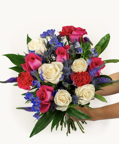 Vibrant bouquet featuring red and white roses, blue delphiniums, and lush greenery.