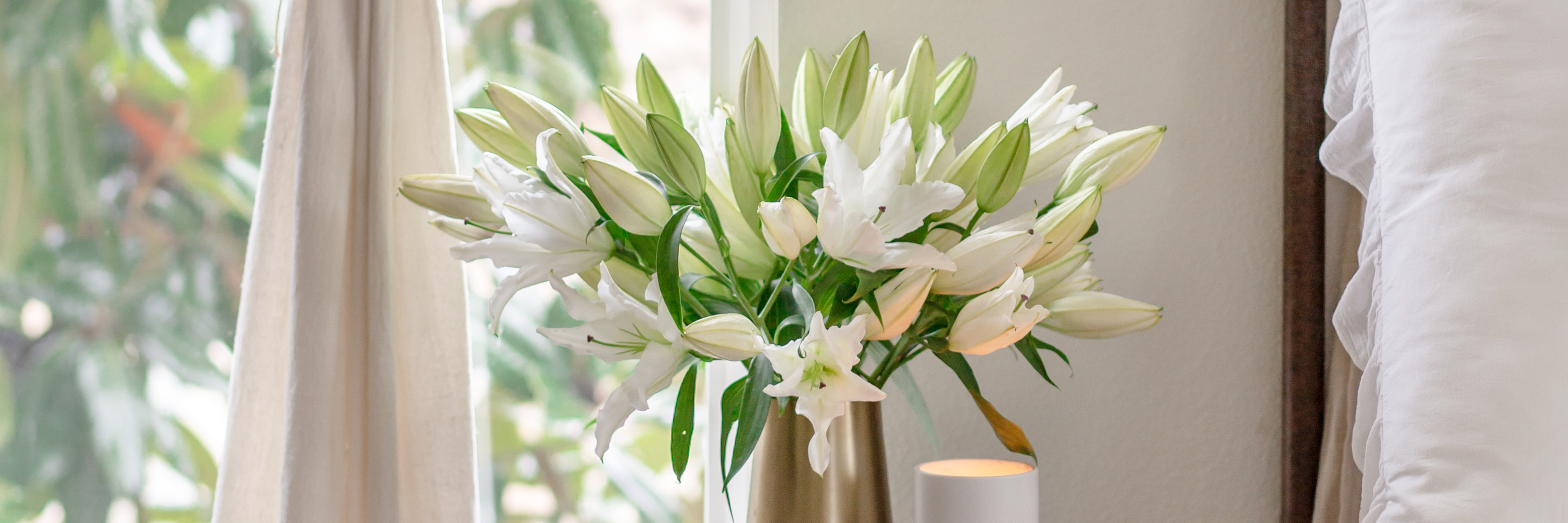Elegant white lilies arranged in a gold vase, brightening up a cozy indoor space.