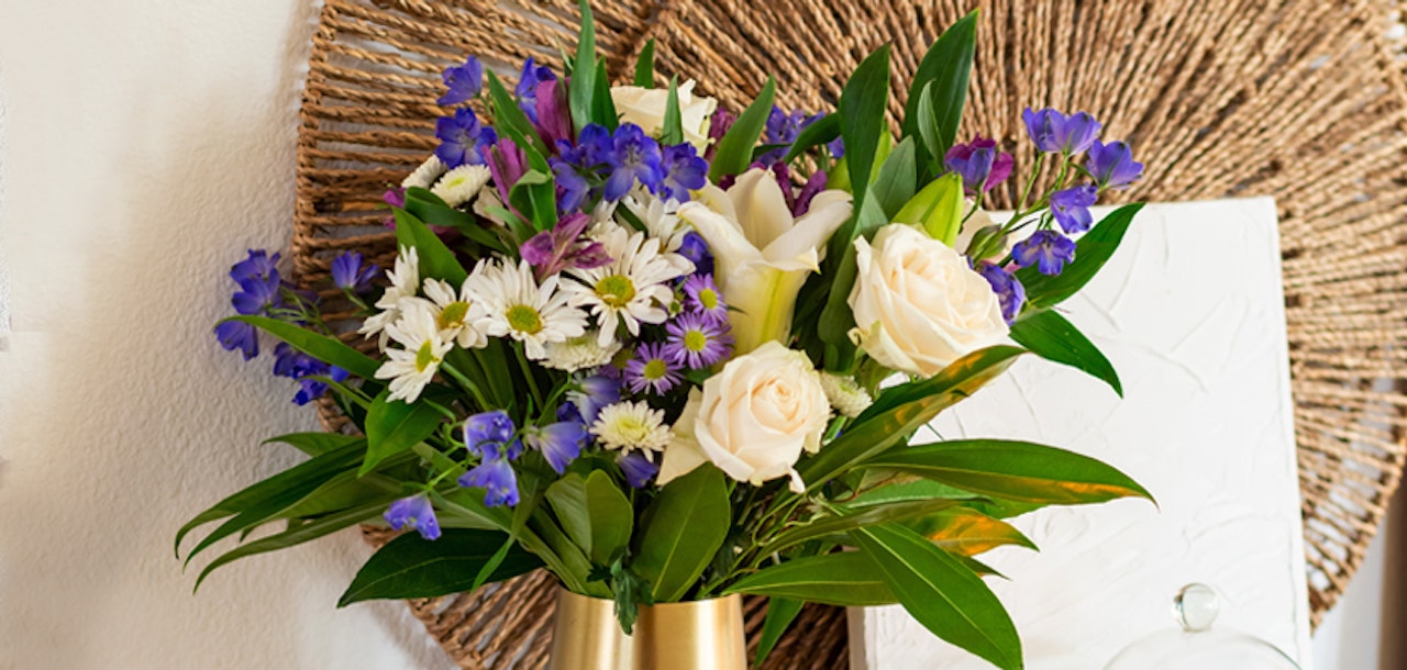 Elegant bouquet featuring white roses, daisies, and vibrant purple blooms in a stylish vase.