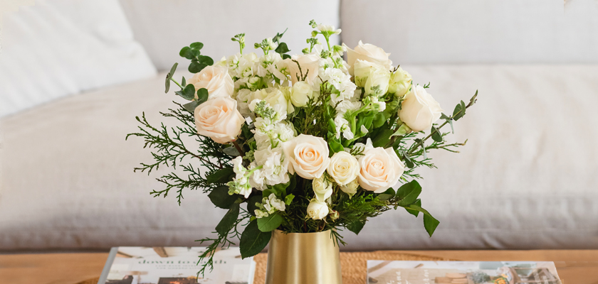 Elegant bouquet of soft peach roses and lush greenery in a stylish golden vase.