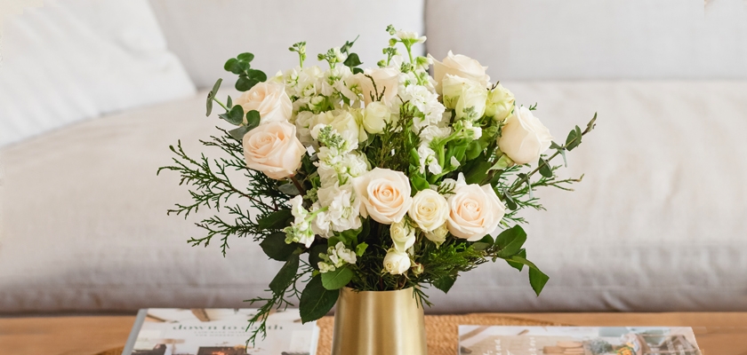 Elegant bouquet of soft peach roses and lush greenery in a stylish golden vase.