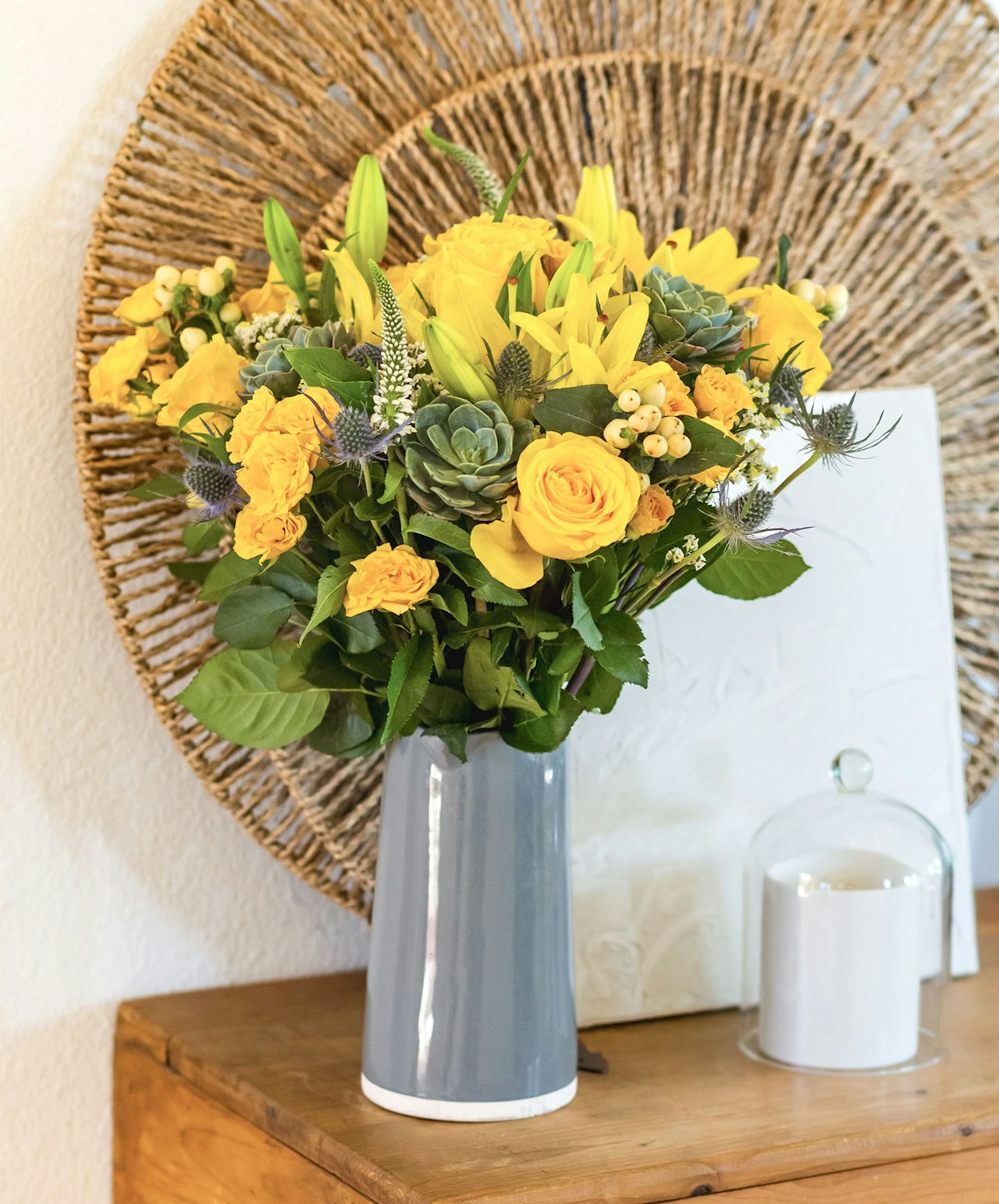 Bright yellow roses and sunflowers in a stylish grey vase, accented with greenery and unique blooms.