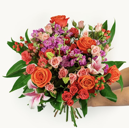 Vibrant floral bouquet featuring orange roses, pink blooms, and lush greenery, elegantly arranged.