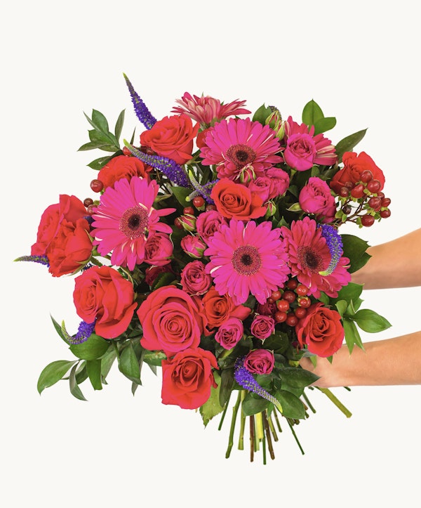 Vibrant bouquet of flowers including red roses, pink gerberas, and purple accents with lush green leaves against a white background, ideal for special occasions.
