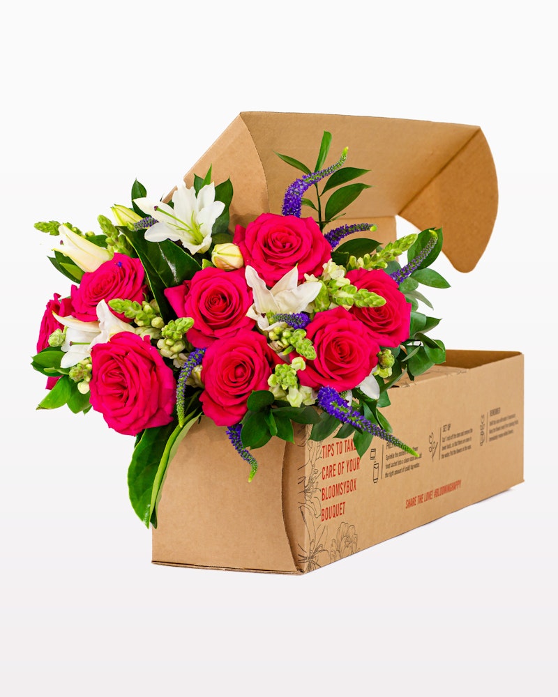 Vibrant bouquet of pink roses and white lilies with greenery packaged in a brown cardboard flower box, ready for delivery or gifting.
