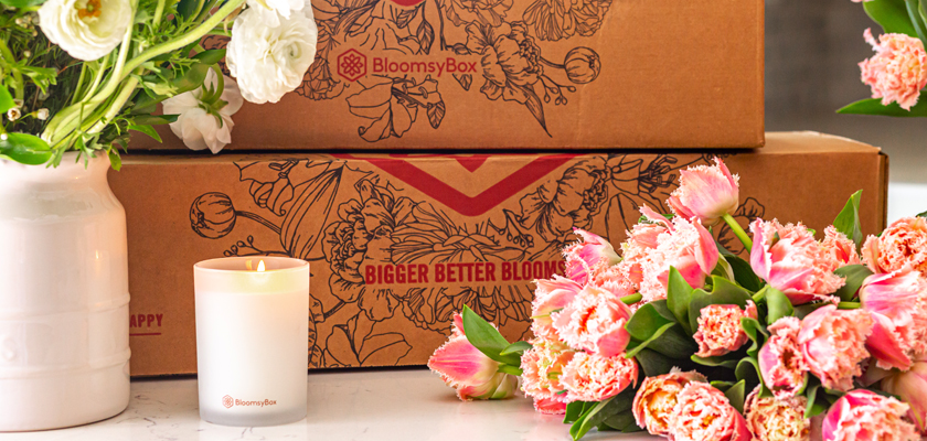 Brightly colored tulips and peonies beside a scented candle and elegant packaging.