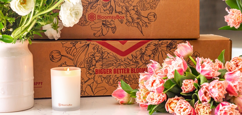 Brightly colored tulips and peonies beside a scented candle and elegant packaging.