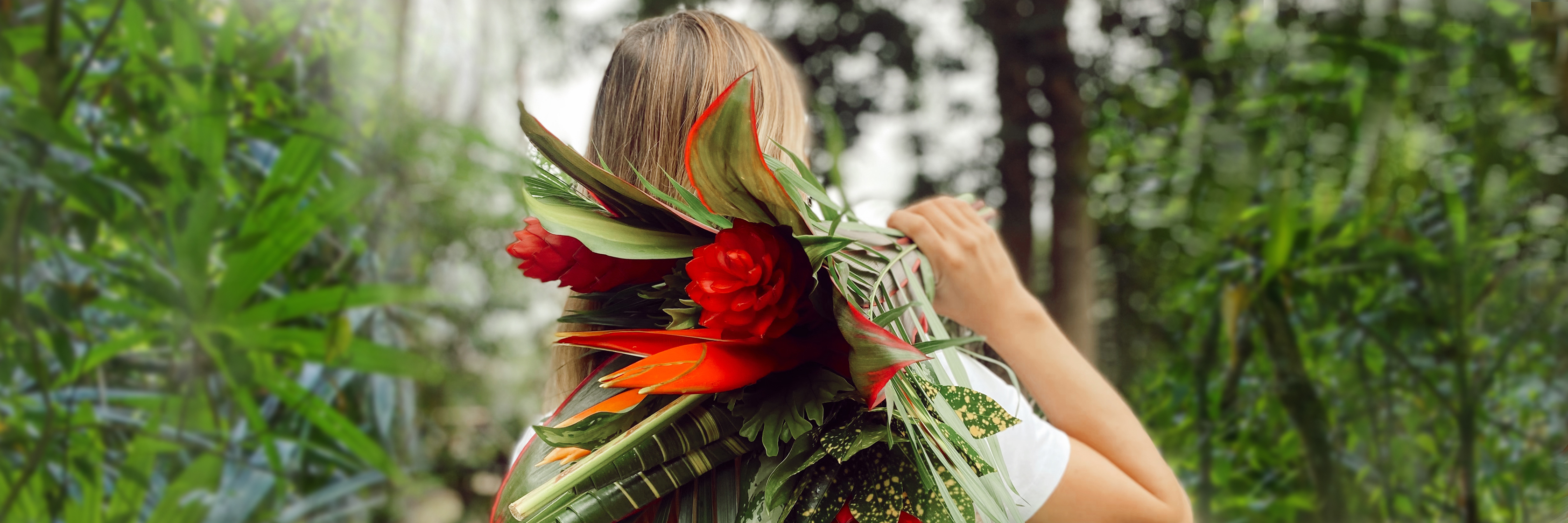 A woman carrying a vibrant bouquet of tropical flowers amidst lush greenery.