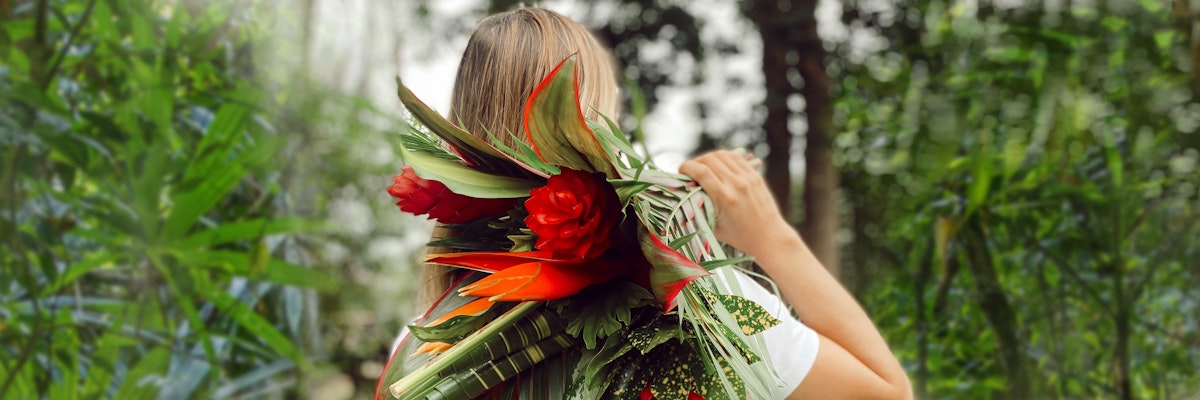 A woman carrying a vibrant bouquet of tropical flowers amidst lush greenery.