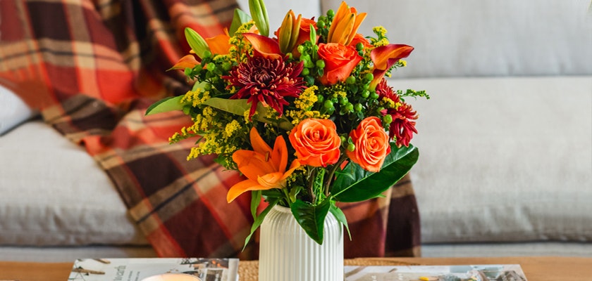 Vibrant bouquet featuring orange lilies, roses, and deep red blooms in a stylish vase.