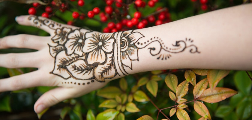 Elegant henna design featuring floral patterns on a hand against a backdrop of vibrant greens.