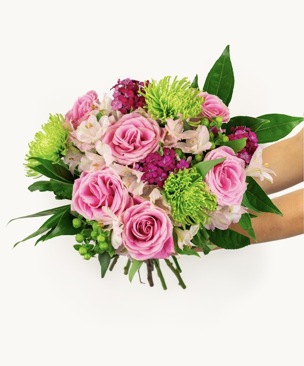A vibrant bouquet of pink roses, green chrysanthemums, and various purple flowers held by a person against a white background, showcasing a mix of blossoms and foliage.