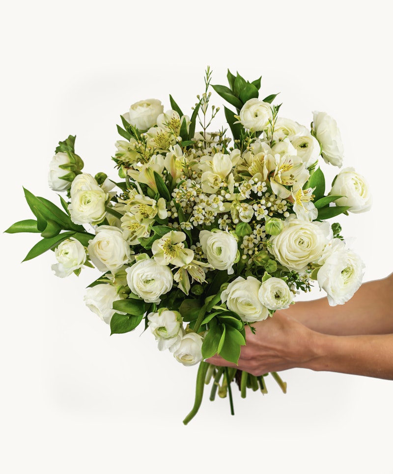 Person holding a beautiful bouquet of white flowers, featuring roses, lilies, and other greenery against a clean white background.