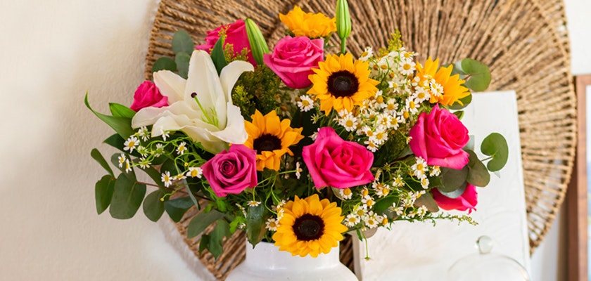 Vibrant floral bouquet featuring pink roses, sunflowers, and white lilies in a chic vase.